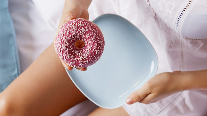 Woman eating a delicious pink donut in the bed