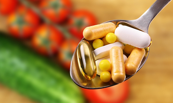 spoon with tablets and capsules on vegetables background